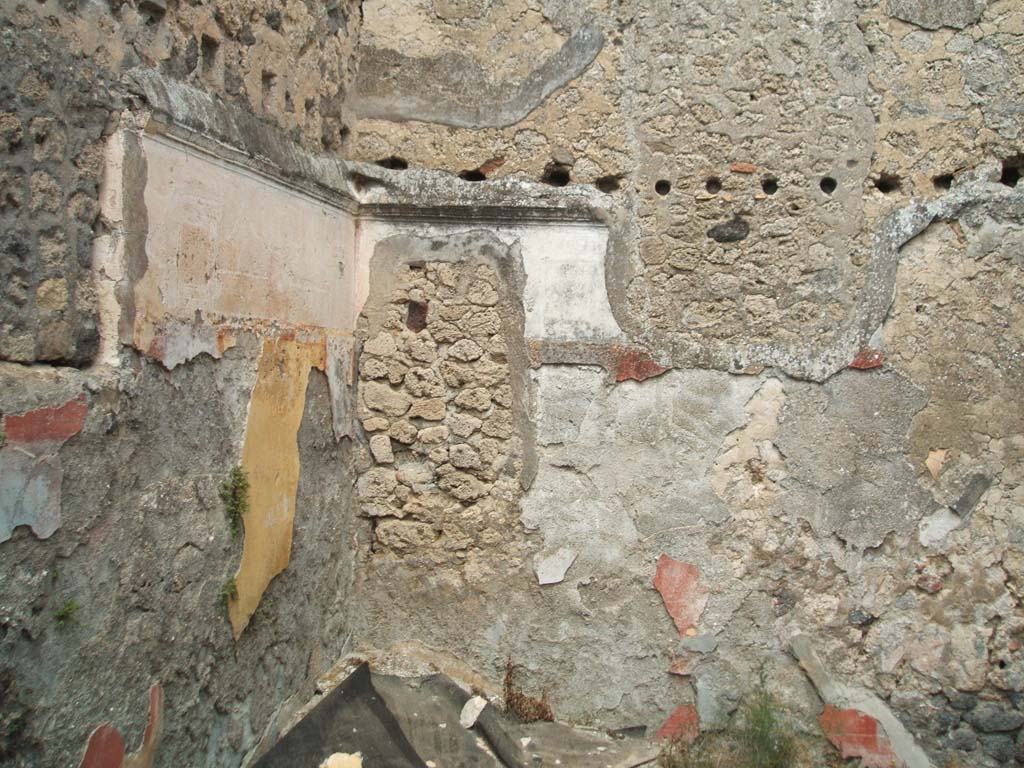 V.2.d Pompeii. May 2005. Room “m”, looking towards the north-east corner of the triclinium.
The blocked window in north wall overlooked V.2.i and was blocked after excavation.
The holes for the support beams of an upper room can be seen in the walls.
This upper room would have been reached by the masonry steps against the east wall in the previous photos.
In the remains of the yellow panel of the north wall, just visible in the centre would have been a painting of monochrome green glass vases on a yellow background.
According to PPM, the middle zone of the north wall was decorated with yellow side panels, and a red panel in the centre edged with “carpet” border and separated by black compartments with painted cane/reeds. On the white upper zone would have been architecture and painted garlands together with a stucco cornice.
Not a lot remains of the decoration of the east wall.