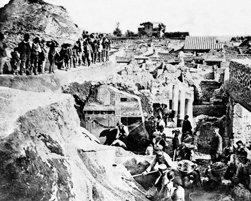 V.2.i Pompeii. Late 19th century photograph showing excavation, (c.1896).
The second style decoration on south wall of Corinthian oecus, room 21 can be seen in the centre.
Looking south from south-east corner of V.2.i, across the columns of the peristyle garden of Casa di Orione/V.2.15, towards the rear of the Casina dell’Aquila in the distance. Photo courtesy of Rick Bauer.