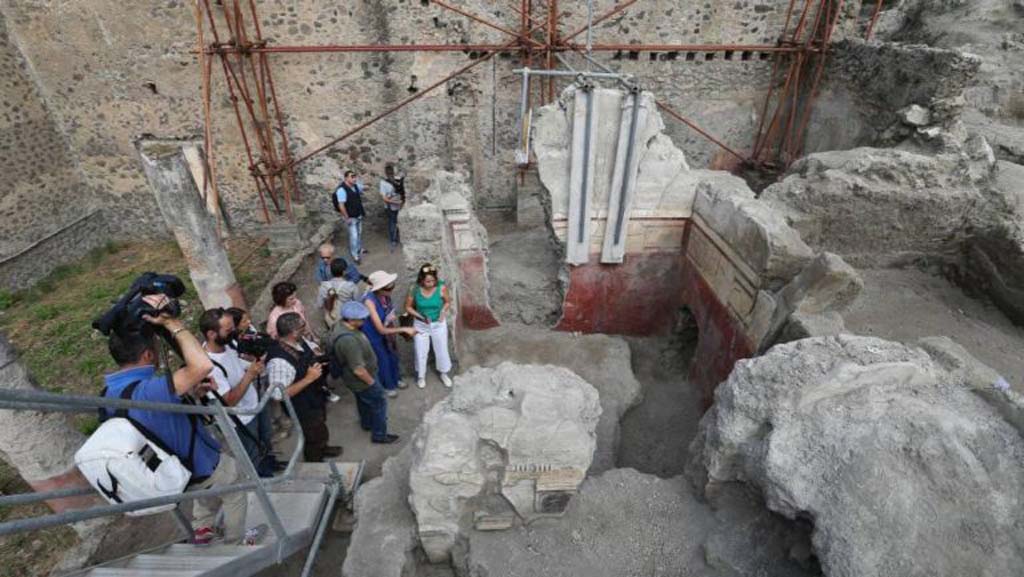V.2.Pompeii. Casa di Orione. August 2018.
Looking north towards room A10, a triclinium (upper right of photo).
This room was the largest of the house, rectangular in shape.
Numerous traces of burnt wood were discovered here in the lapilli, and signs of a fire can be seen on the decoration of the east wall.
See Osanna M, 2019. Pompei. Il tempo ritrovato. Le Nuove Scoperte. Milano: Rizzoli (p. 106).
In the centre is room A6, garden area 11c is on the left, and portico A19 is full of people.
Room A18, north ala, is on the centre right.
Photograph © Parco Archeologico di Pompei.