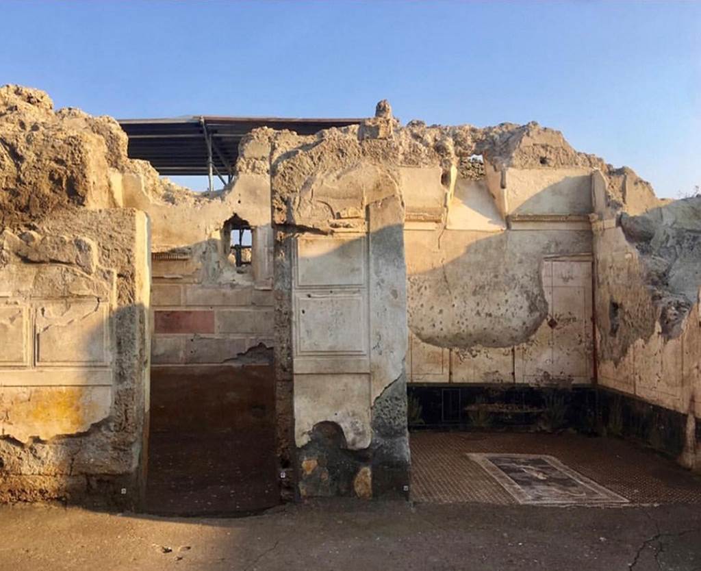 V.2.Pompeii. Casa di Orione. March 2019.
Looking south across atrium towards doorway to room A11 (left) with first style decoration.
Room A13, the south ala, is to the right.
Photograph © Parco Archeologico di Pompei.
The doorway to room A11 would have had a door (as shown by the two typical recesses visible along the jambs in parallel limestone blocks, just over a metre and a half above the ground level, functional to the lodging of the closing pole/stake/bolt, and a high window opening in the south wall which took light from an open area of the nearby House of Adonis (V.2.21).
This room would have been used as a cubiculum, although at the time of the eruption it may have been used for something else.
The walls contained many holes (which together with hinges and iron nails found in the lapilli) indicated the presence of shelves and shelving, so possibly the room was being used as a storeroom.
See Osanna M, 2019. Pompei. Il tempo ritrovato. Le Nuove Scoperte. Milano: Rizzoli (p. 100).