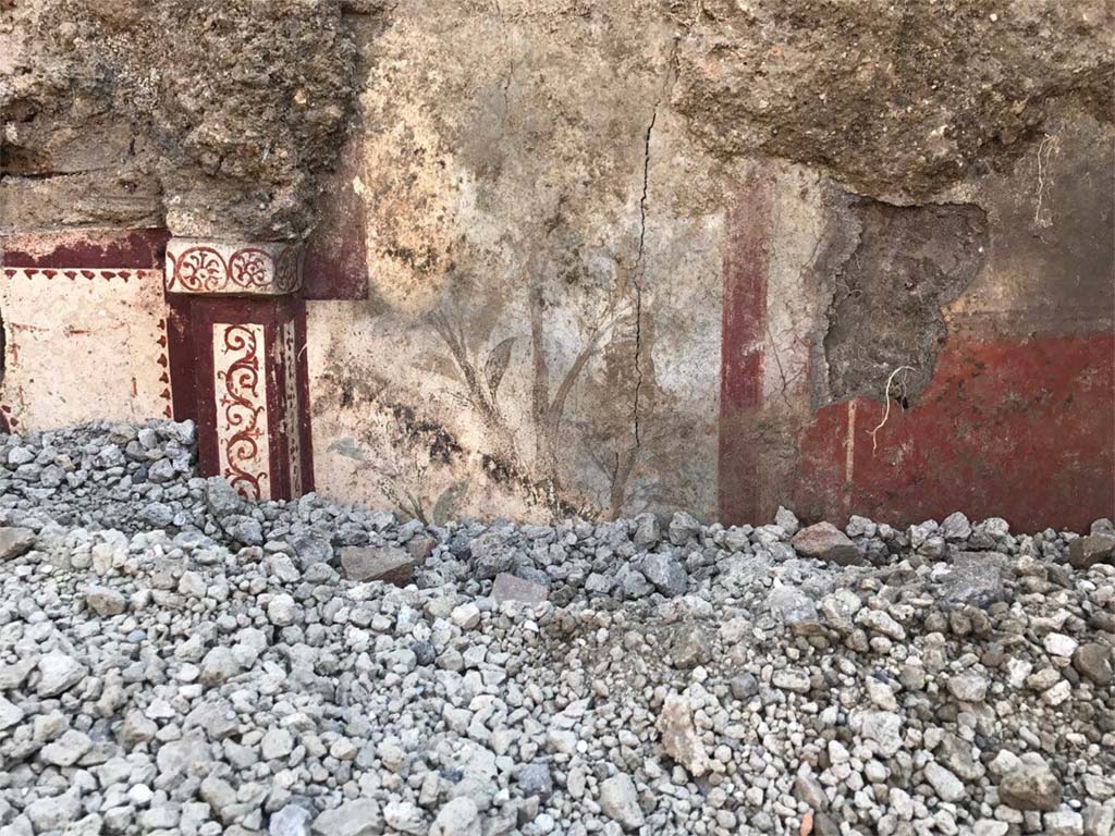 V.3.13 Pompeii. 2018. Room 2a. East wall. A sumptuous painted lararium begins to emerge from the lapilli in a room which was being excavated.
On the left is the edge of the niche and right is painting of flowers.
Parete est. Un sontuoso larario dipinto inizia ad emergere dai lapilli in una stanza che è stata scavata.
A sinistra è il bordo della nicchia e a destra è dipinto di fiori.
Photograph © Parco Archeologico di Pompei.