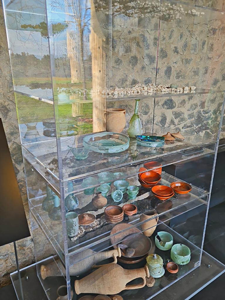 V.3.13 Pompeii. March 2024.
Reconstruction of a cupboard/cabinet (originally made of wood) with its original contents, found in this house. There was a large amount of crockery mainly pottery and glass. On shelves 3 and 4 are the remains of carbonised wooden planks.
Ricostruzione di un armadio/mobile (originariamente in legno) con il suo contenuto originale, trovato in questa casa. C'era una grande quantità di stoviglie, principalmente ceramiche e vetro. Sugli scaffali 3 e 4 ci sono i resti di assi di legno carbonizzato.
On display in Palaestra in exhibition entitled – “L’altra Pompei, vite comuni all’ombra del Vesuvio”.
Photo courtesy of Giuseppe Ciaramella.
