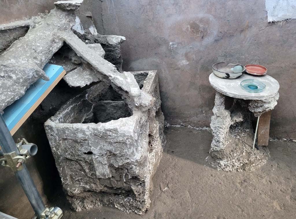 V.3.13 Pompeii. 2022. Room 3b, bedroom. Cast of wooden chest, table and roof beams.
Alongside the bed was a bipartite wooden chest, left open at the moment when the owners fled, and onto which beams and planks from the ceiling above collapsed.
Accanto al letto era un baule ligneo bipartito, lasciato aperto nel momento della fuga e su cui sono crollati travi e tavole del solaio soprastante.
Photograph © Parco Archeologico di Pompei.
