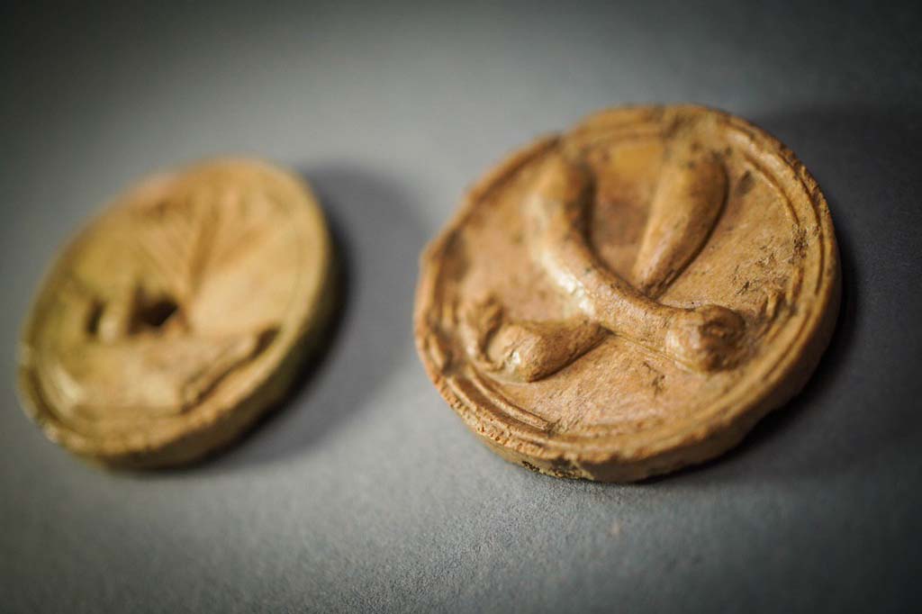 V.3 Pompeii. Casa del Giardino. August 2019. Two bone buttons. On the one in the foreground there are two courgettes.
Due bottoni in osso. Su quello in primo piano ci sono due zucchine.
Photograph © Cesare Abbate/ANSA courtesy Parco Archeologico di Pompei.