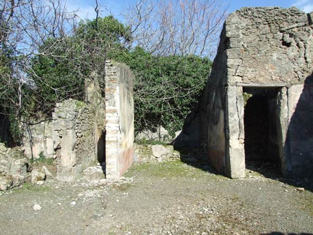 V.4.c Pompeii. March 2009. Room B, the atrium, looking east. Looking across atrium to doorways to room F, on left, room J, corridor to garden, room G, tablinum, and room H, cubiculum. When excavated the atrium had flooring similar to that of the fauces, opus signinum/cocciopesto.
V.4.c Pompeii (described as second house after that of Lucrezio Frontone).
Found on 15th March 1902, between the upper layers of a room near the tablinum, was an oxidised statuette (100mm high) of a bearded and crowned Hercules, leaning with the weight of his body on his right leg, since the left leg was slightly bent. In his right hand he held the club pointing downwards, and in his left hand he held the apples of the Hesperides; the lion’s skin was hanging on his left forearm. If he was beardless, he would have very closely resembled the Hercules Righetti of the Vatican Rotunda. Also found were – a bronze cylindrical bell with an iron ringer/clapper. An oxidised medium and small bronze coin. A glass bottle with a spherical belly. Found on the 24th March in the same place was a terracotta single-burner lamp, with a ring handle. See Notizie degli Scavi di Antichità, 1902, (p.213)