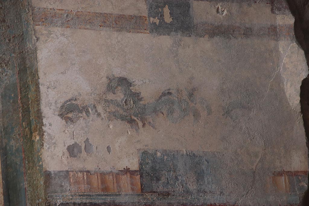 V.6.12 Pompeii. October 2024.
Detail of dolphin and marine animal from upper panel on east side of central painting of Priapus. Photo courtesy of Klaus Heese.