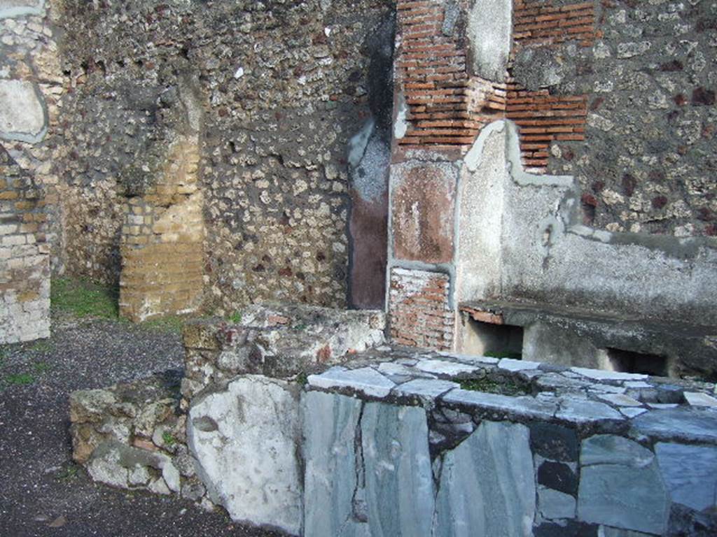 VI.3.20 Pompeii. December 2005. Counter with hearth at end. According to Dyer:
“At the angle of two streets, just behind the fountain, was a small shop, called by some a thermopolium, or shop for the sale of hot drinks. The walls were gaudily painted in blue panels with red borders, and towards the street was a counter cased with marble. The stains left on these counters, apparently by wet drinking-glasses, have led to the identification, or supposed identification, of several such shops.”
See Dyer, T., 1867. The Ruins of Pompeii. London: Bell and Daldy. (p.49)
According to Breton: This bar of Fortunata had a counter of masonry which held several large terracotta containers, and was covered with a marble tablet, where the footprints of cups/glasses could still be recognised. The liquids contained in them must have contained some acid principle which had attacked the polish of the marble. At the rear was a higher area which held the brazier for heating various beverages.”
See Breton, E; Pompeia, decrite et dessine, 1855, (p.219)