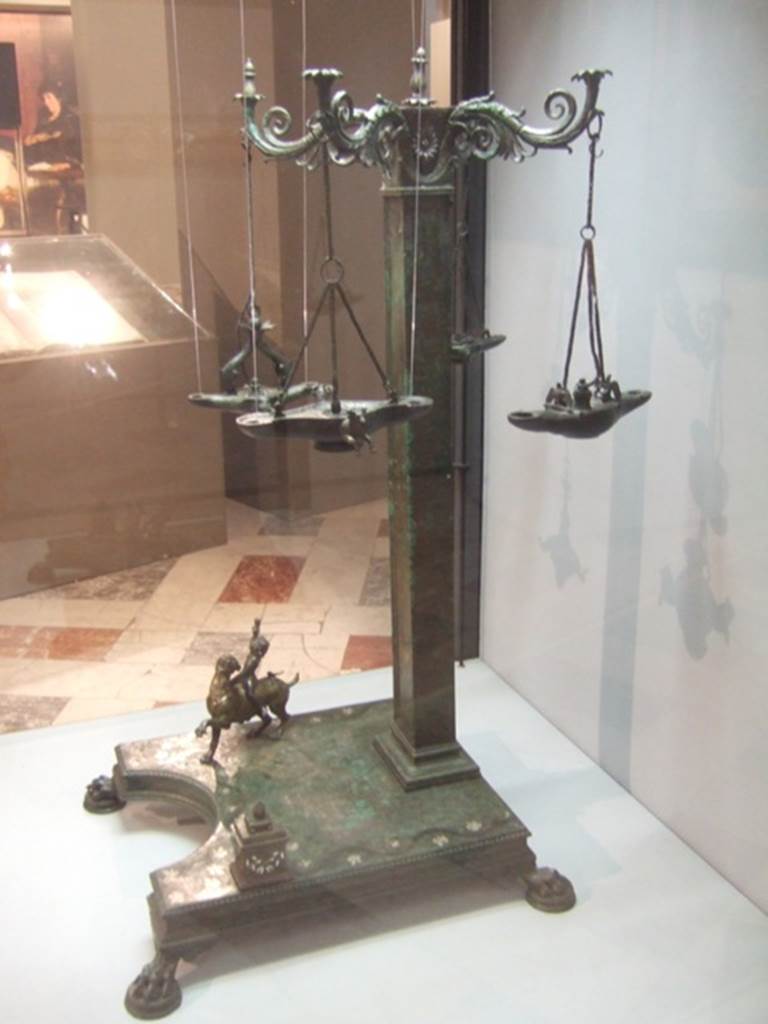 Found 19th August 1813 in VI.6.1 Pompeii. Bronze candelabrum with four volute branches for lamps.
Now in Naples Archaeological Museum. Inventory number 4563.
According to Pagano and Prisciandaro, an elegant bronze lamp was found in the portico of the garden.
See Prisciandaro, R., 2006. Studio sulle provenienze degli oggetti rinvenuti negli scavi borbonici del regno di Napoli. Naples: Nicola Longobardi.
(p. 109, reported 9th September 1813, PAH I, 3, 127, add. 271, and p.109, reported 23rd December 1813, PAH I, 3, 139, add. 271,72).
According to Kuivalainen, this lampstand was discovered in the portico of the peristyle together with the bronze statue of two males, H13 see below).
He comments –
“This lamp has both a religious and a practical purpose. The pictorial programme of the lamp is quite obviously dedicated to Bacchus – the child riding a panther, the mask, the bull as one of his characteristic animals, all speak for this. Choosing a child Bacchus was relatively original due to his rare appearance in visual arts in general, but it may share the idea of growth and fertility with a rhyton, a she-panther, not to omit the idea of light in the worship of Bacchus. Perhaps this lampstand was used for private worship. On the practical side, the asymmetrical placement of the pillar made more space for a vessel with oil for filling the lamps.”
See Kuivalainen, I., 2021. The Portrayal of Pompeian Bacchus. Commentationes Humanarum Litterarum 140. Helsinki: Finnish Society of Sciences and Letters, (H18, p.222).