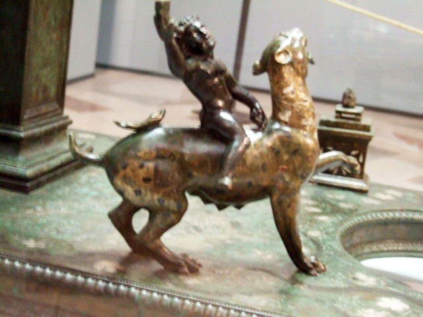 Bronze statuette of Dionysus mounted on his panther on the base of a candelabrum.
A small altar is in the background. Found in VI.6.1 Pompeii. Now in Naples Archaeological Museum.