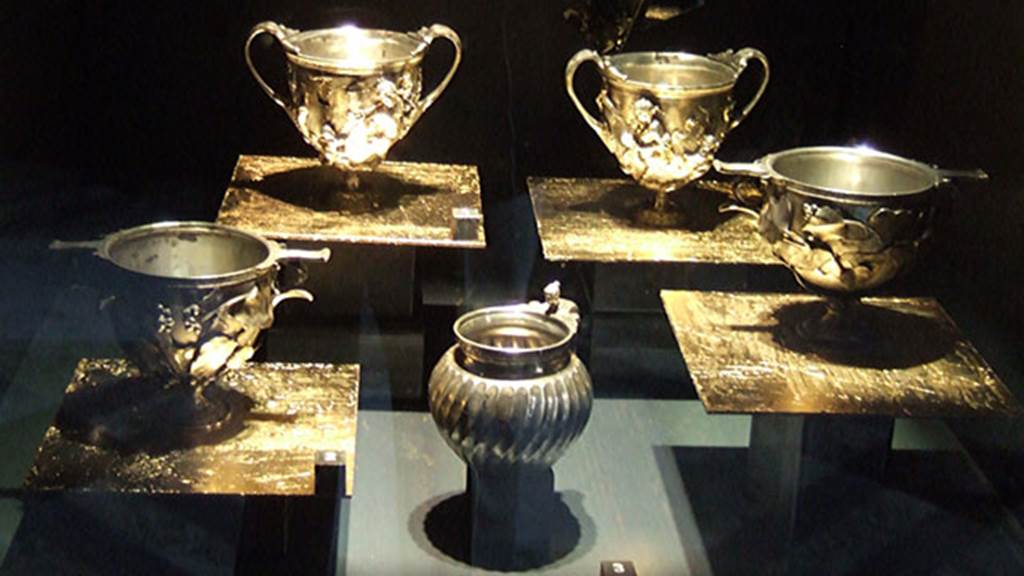 VI.7.20 Pompeii. Silver found on 23rd March 1835 in a room on the left (south) of the Tuscan atrium.
2 Canthari, cups with high handles, decorated with Centaurs and Amorini (rear). Inventory numbers 25376 (left) and 25377 (right).
2 Scyphi, deep oval cups with two handles, with ivy leaves decorations with traces of gilding (front right and left). Inventory numbers 25378 (left) and 25379 (right).
An olpe, a round mouthed oil flask or jug, with female head (front centre). Inventory number 25372.
Now in Naples Archaeological Museum.
See Pagano, M. and Prisciandaro, R., 2006. Studio sulle provenienze degli oggetti rinvenuti negli scavi borbonici del regno di Napoli. Naples : Nicola Longobardi. (p.150).
See Guzzo, P. (A cura di), 2006. Argenti a Pompei. Milano, Electa. (pages 114-122), figs. 106-109.