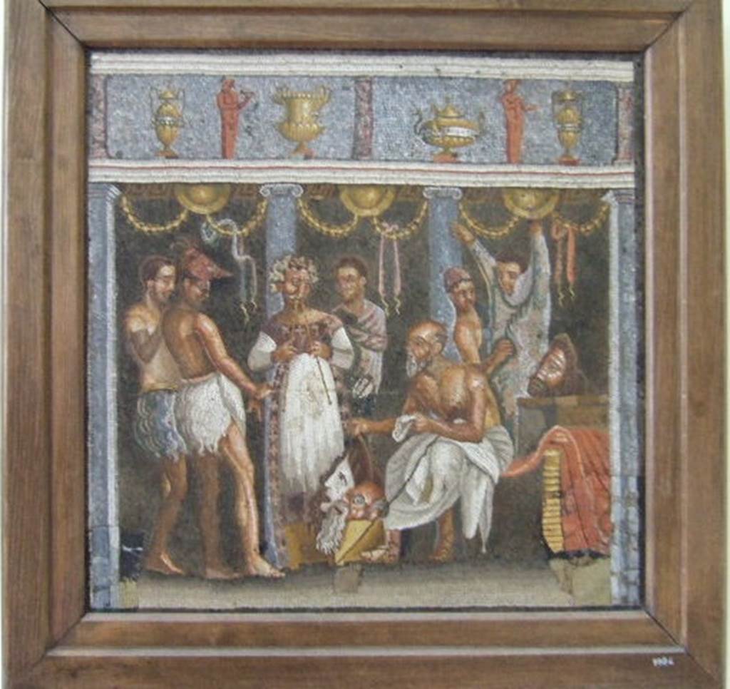 According to Mau this is a mosaic of an actor making preparations for the stage and was found in the floor of the tablinum. The label in the museum says it was found in the tablinum of VI.8.3. Now in Naples Archaeological Museum. Inventory number 9986. See Mau, A., 1907, translated by Kelsey F. W. Pompeii: Its Life and Art. New York: Macmillan. (p. 314)