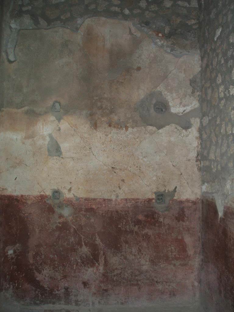 VI.8.23 Pompeii. May 2005. Room on north side of atrium.
Remains of simple wall painting from north wall, a painted red dado (zoccolo) with white painted upper wall but lacking any decoration.
All around the wall at regular intervals, some holes were drilled for shelving supports.