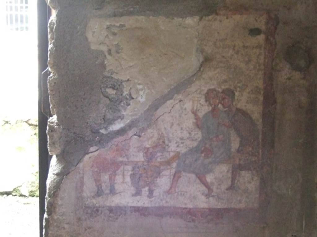 VI.10.1/19 Pompeii. March 2009. Fresco on west wall of rear room, on north side of doorway.
Two men in tunics and wearing shoes sit at a table.
A man in a blue tunic sits on a bench and a man in a brown tunic leans over him.
See Helbig, W., 1868. Wandgemälde der vom Vesuv verschütteten Städte Campaniens. Leipzig: Breitkopf und Härtel. (1504; p369).