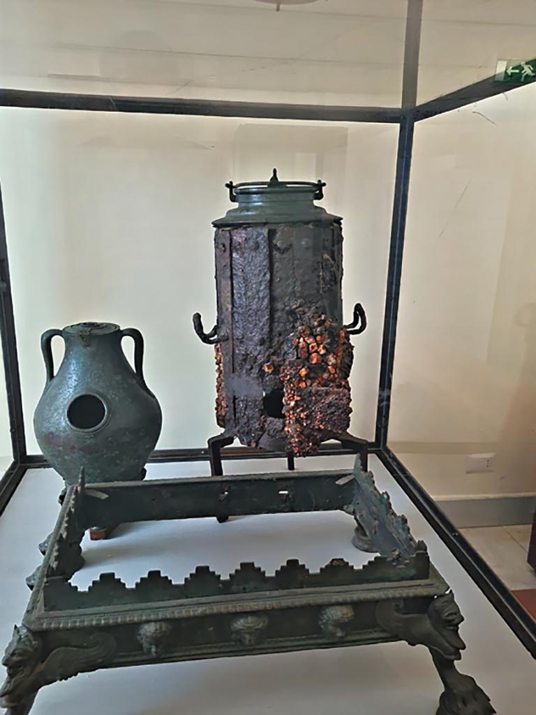 VI.12.2 Pompeii. September 2024.
Display case with items – Portable bronze brazier, Stove and bronze chafing dish.
Now in Naples Archaeological Museum. Photo courtesy of Giuseppe Ciaramella.