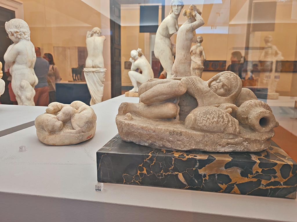 VI.12.2/5 Pompeii. October 2023.
Marble block modelled into four puppies, on left, found near small stairs 21/5/1895, inv. 124829. Photo courtesy of Giuseppe Ciaramella.
On the right is the marble statuette of a small sleeping fisherman found in VI.8.23, inv. 6509.
On display in “L’altra MANN” exhibition, October 2023, at Naples Archaeological Museum.