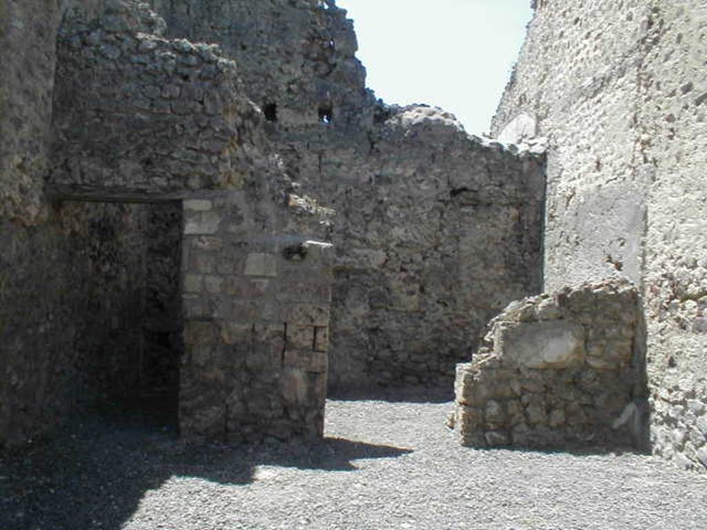 VI.14.24 Pompeii. May 2005. Looking west across shop to doorways to two rear rooms.
According to BdI, on the right of the shop entrance in the north-east corner, was a small hearth, and in the same corner was a latrine. Objects found in the shop were a bell, various pots, five keys and a few bronze coins. The rear room on the right was the biggest.
Upon excavation, the walls of the upper rooms were also preserved, one above the rear rooms, the other above the shop-room. This last wall, with pink coloured plaster until the height of approximately 1.50m, unpainted above, and with a large window onto the roadway. It was evident that these two rooms joined by a doorway between them, formed a separate complex from the rest of the house, and that this could be rented independently from the shop below. See Bullettino dell’Instituto di Corrispondenza Archeologica (DAIR), 1876, (p.44)