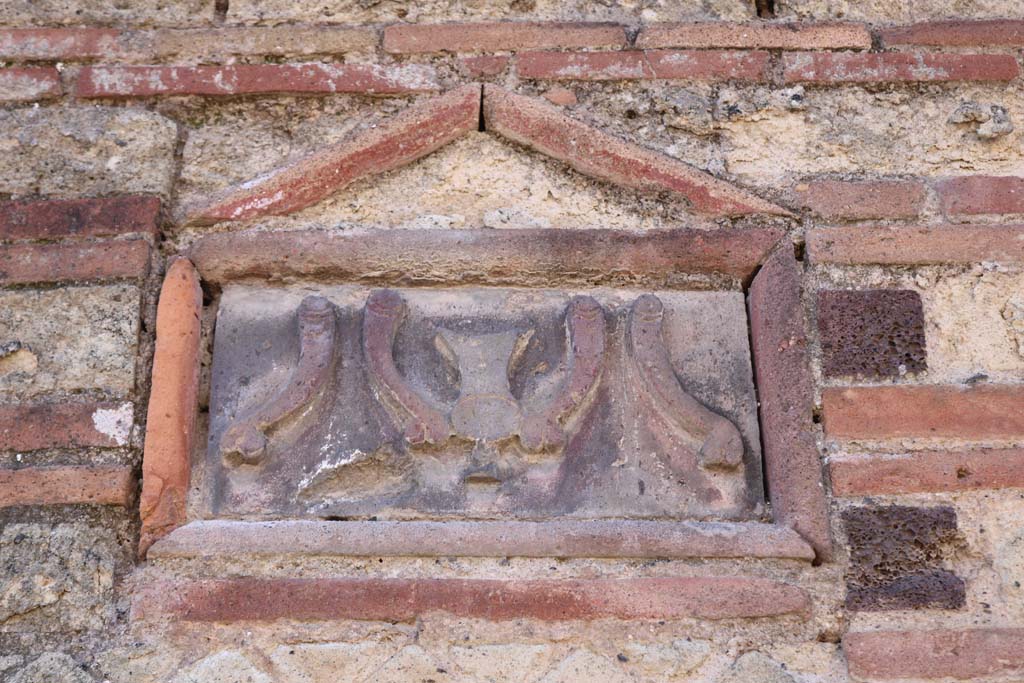 VI.14.28 Pompeii. December 2018. 
Plaque on outside wall showing a “fritillus” between four phalluses. A fritillus was the vessel for dice-throwing. Photo courtesy of Aude Durand. 
