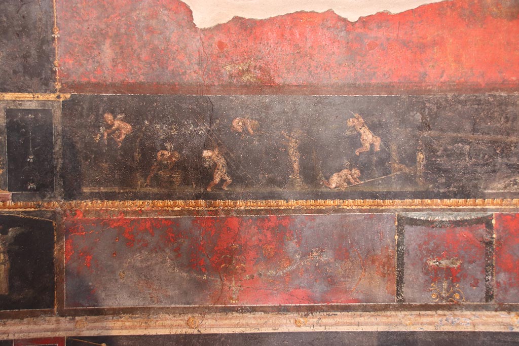 VI.15.1 Pompeii. October 2024.
Predella in centre of north wall, painted panel of cupids gathering and pressing grapes. Photo courtesy of Klaus Heese.