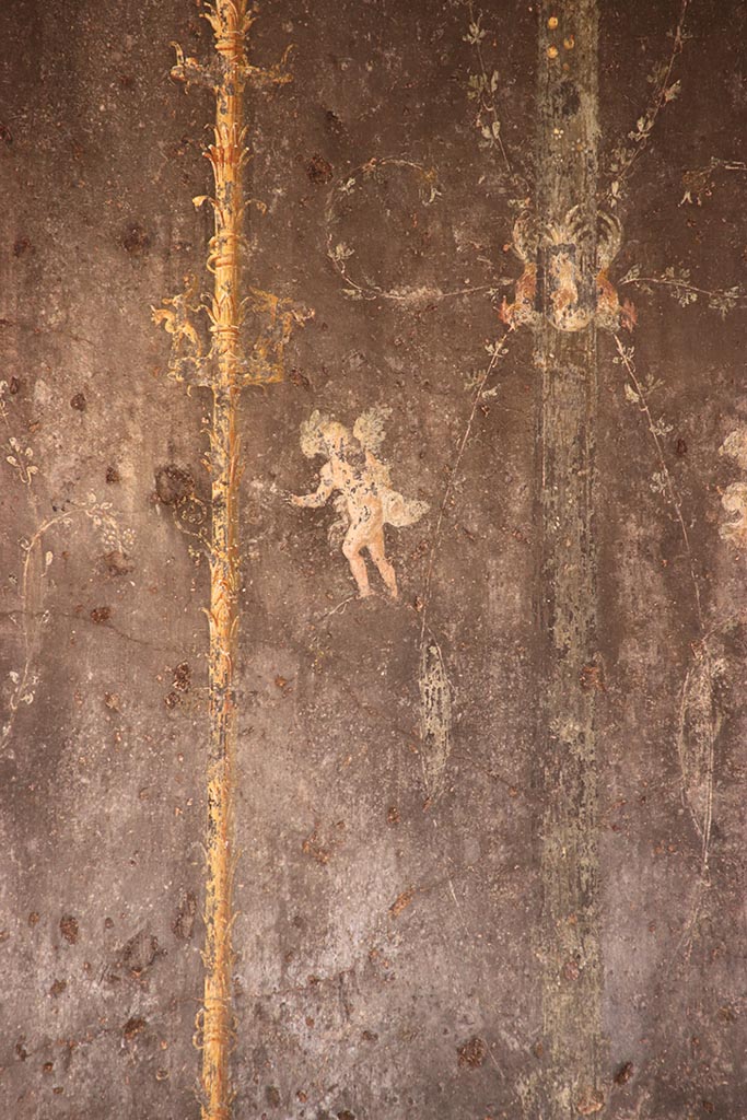 VI.15.1 Pompeii. October 2024.
Detail of cupid from black painted panel with candelabra from east end of north wall.
Photo courtesy of Klaus Heese.