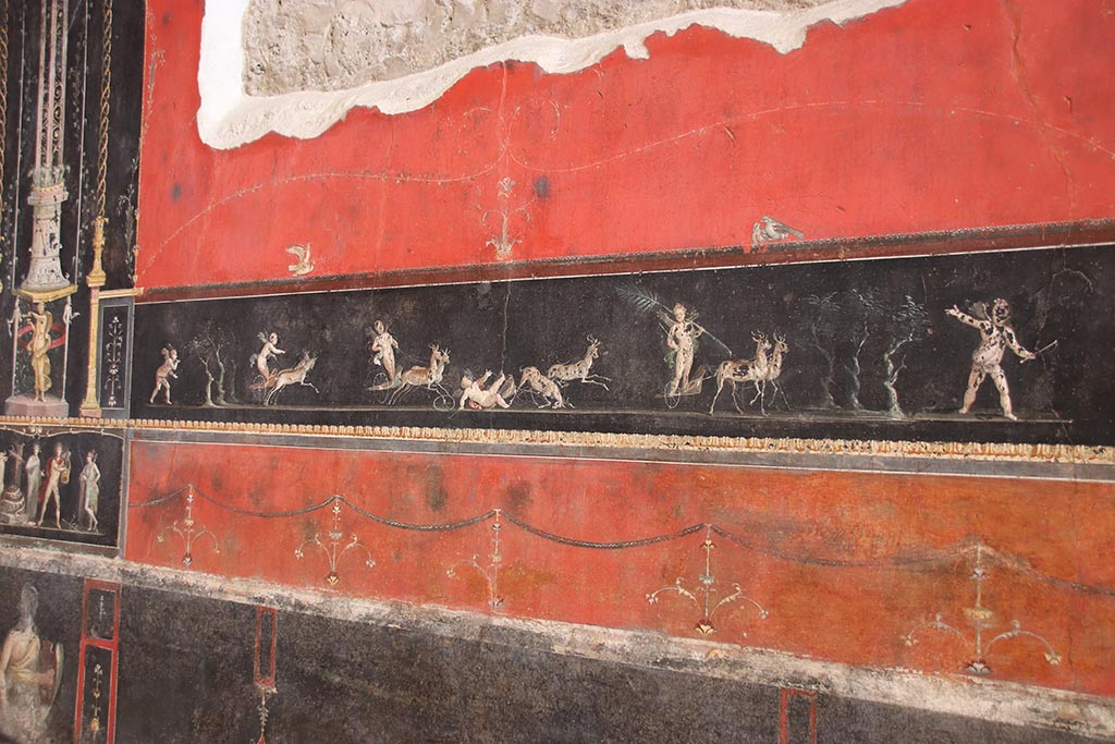 VI.15.1 Pompeii. October 2024.
Centre of east wall with painted panel of cupids in a race between chariots pulled by deer. Photo courtesy of Klaus Heese.
