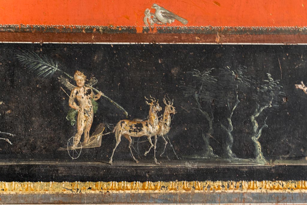 VI.15.1 Pompeii. March 2023.
Lower centre of east wall, detail of part of painted panel - the winning cupid in chariot race. Photo courtesy of Johannes Eber.