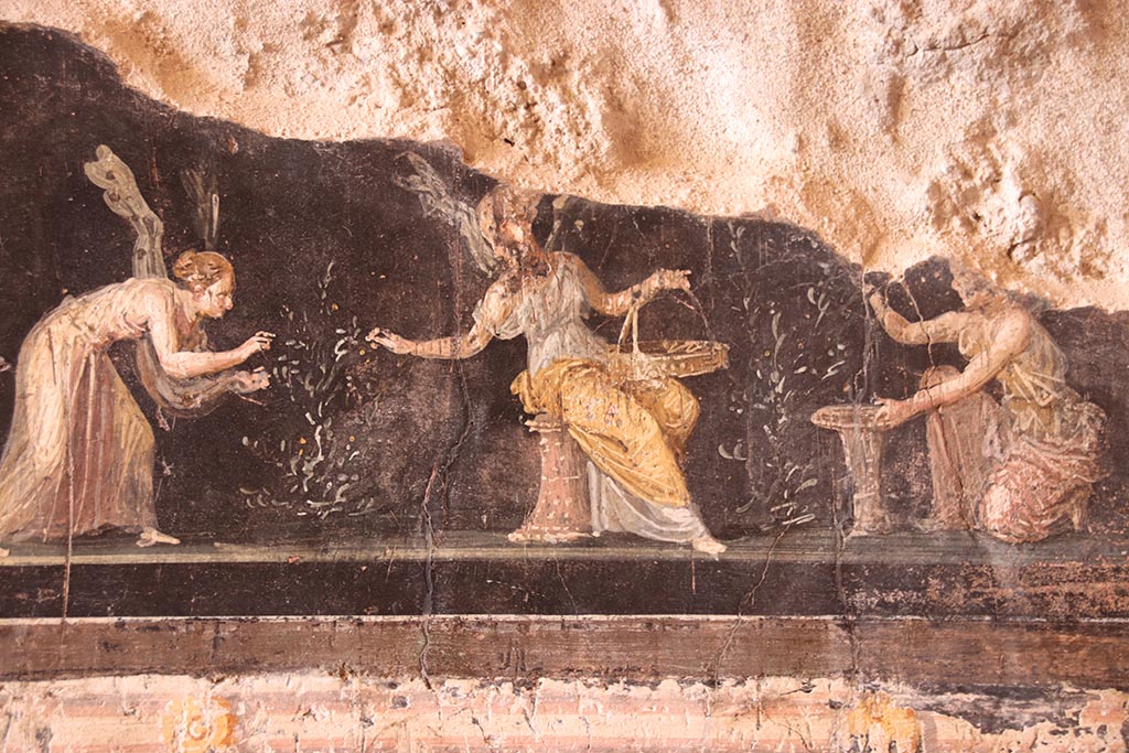 VI.15.1 Pompeii. October 2024.
Predella on west wall in north-west corner with detail of painted panel of three Psychai gathering flowers. Photo courtesy of Klaus Heese.