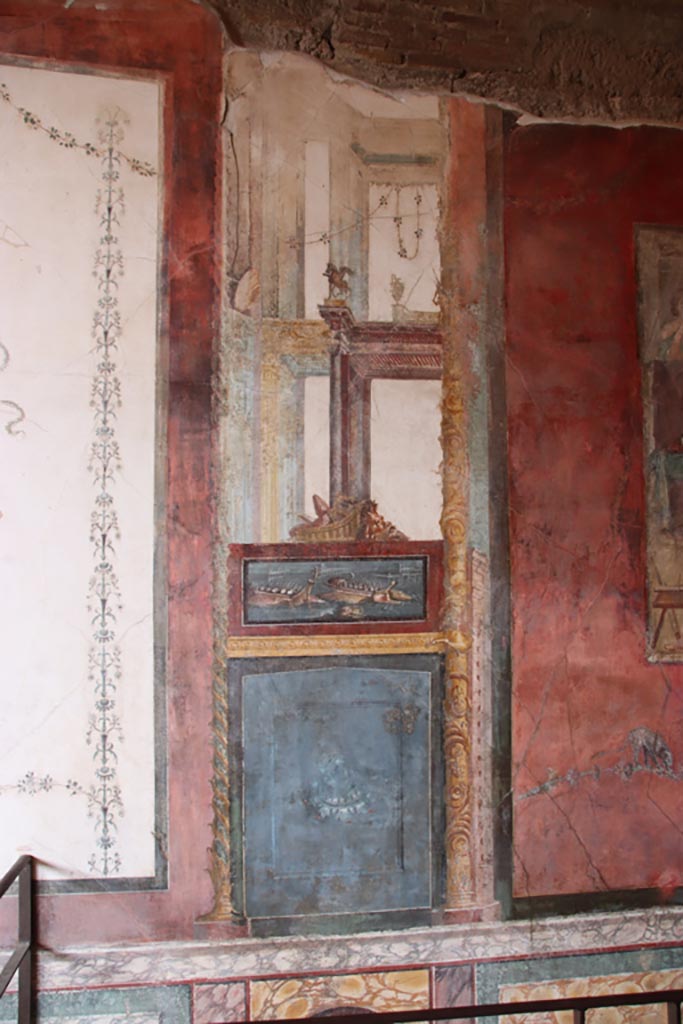 VI.15.1 Pompeii. October 2023.
North wall of exedra on west side of central painting, wall painting of naval scene, with basket and mask above.
Photo courtesy of Klaus Heese.