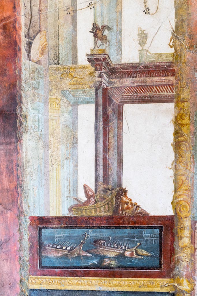 VI.15.1 Pompeii. March 2023.
North wall of exedra, painted panel of naval scene, with basket and mask above.
Photo courtesy of Johannes Eber.