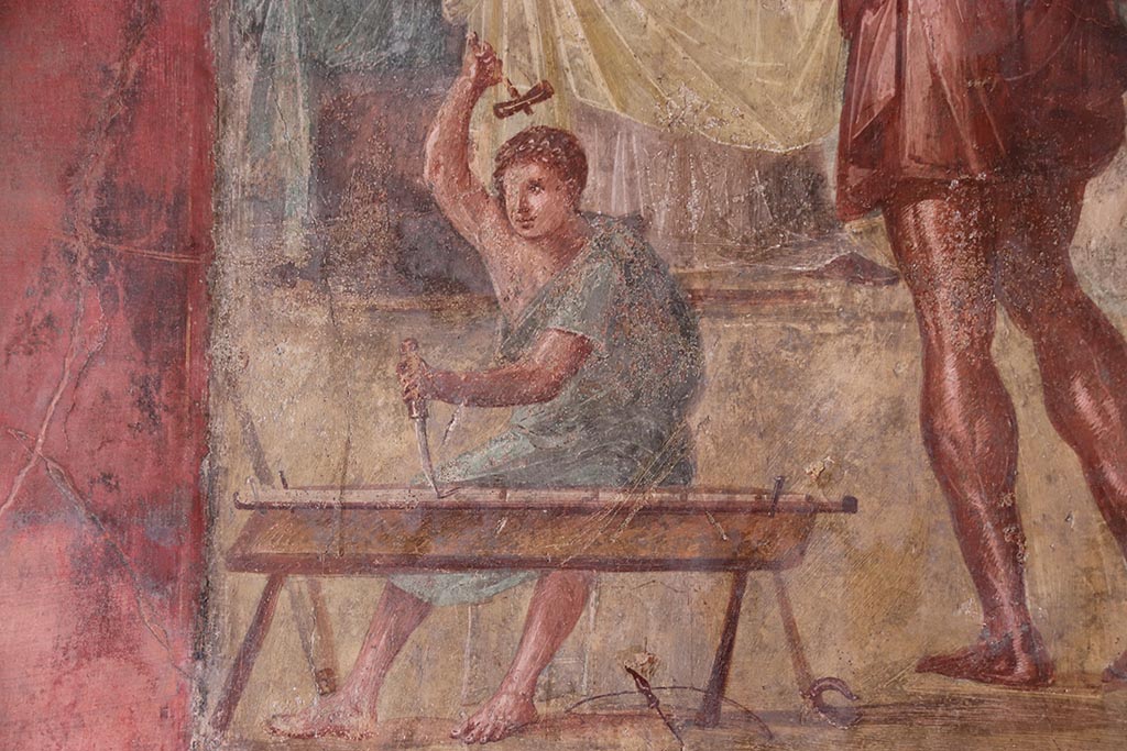 VI.15.1 Pompeii. October 2024.
Detail from central painting showing the helper of Daedalus carrying out work with hammer and chisel. Photo courtesy of Klaus Heese.
