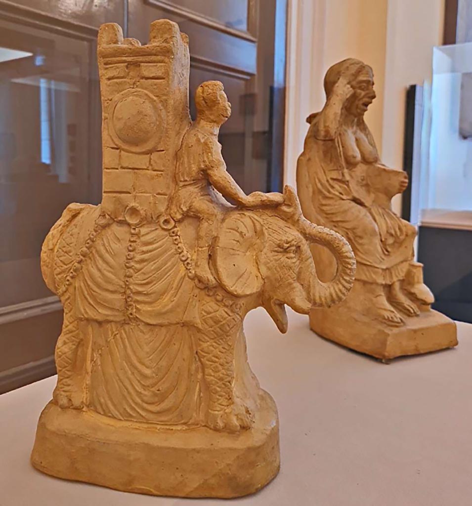 VI.15.5 Pompeii. October 2023.
Clay figurine of an elephant carrying a tower on its back inv. 124845, and clay figurine of an old drunken woman inv. 124844. Photo courtesy of Giuseppe Ciaramella.
On display in “L’altra MANN” exhibition, October 2023, at Naples Archaeological Museum.