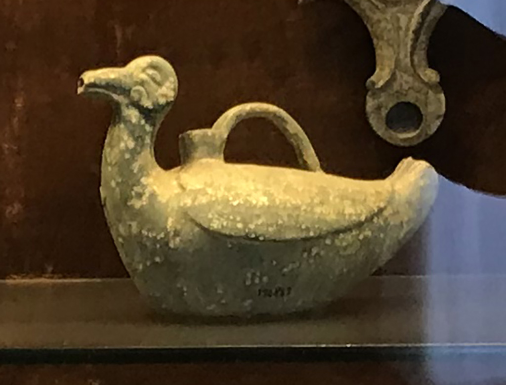 VI.15.5 Pompeii. April 2019.
Pot/jug/vase in the shape of a duck, found on west side of garden near the aedicula. Photo courtesy of Rick Bauer.
Now in Naples Archaeological Museum, inventory no. 124842.
Sala (room) 88, glass cabinet II, shelf B (middle).
Also found with this was a pot/jar/vase in the shape of a bird (inv. 124848), the group of Pero and Mikon (inv.no.124846) and a statue of Silenus (inv.no. 124847 cat 7.1)
See Di Gioia, E. (2006). La ceramica invetriata in area vesuviana. “L’Erma” di Bretschneider, (p.61).