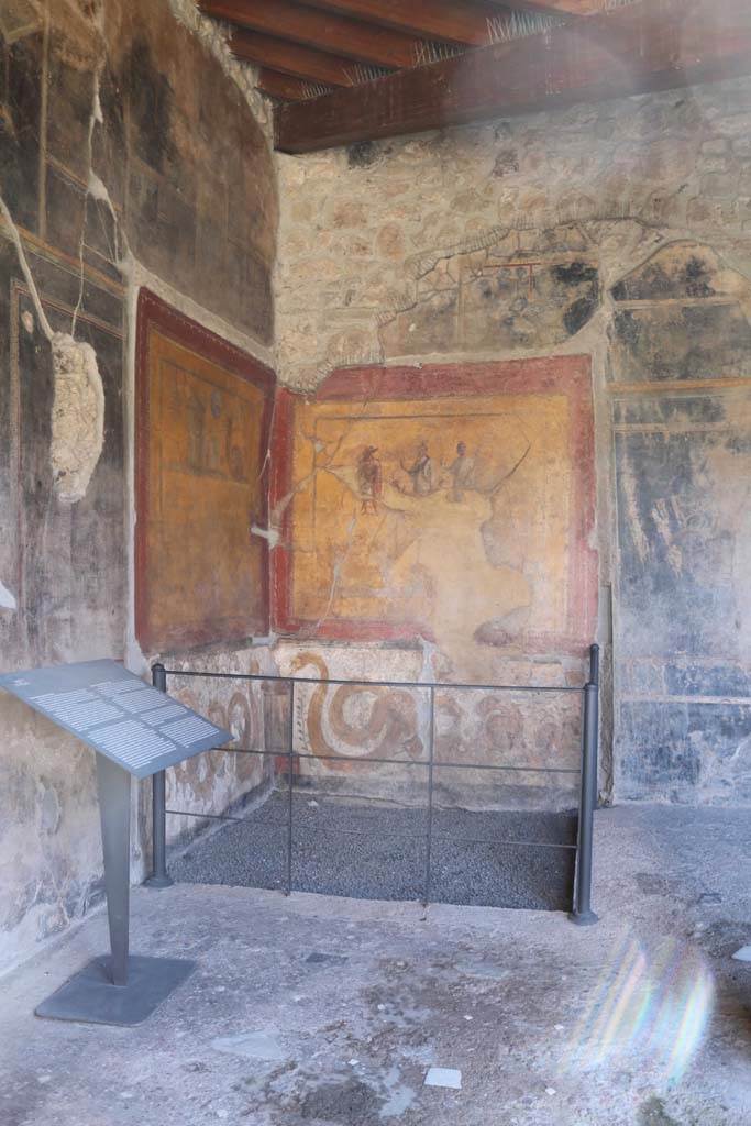VI.16.7 Pompeii. December 2018.
Room F, looking south from east portico towards lararium in south-east corner of peristyle.
The shrine was dedicated to the cult of the Egyptian deities.
On one wall are paintings of objects of the cult of Isis including a sistrum (rattle) and a cobra.
On the other wall is Isis in the centre wearing a red and black sash and holding a sistrum.
Anubis is dressed in red. A small figure between Isis and Anubis is possibly Harpocrates.
Serapis or Osiris is dressed in white with the horn of plenty in his left hand and a sistrum in his right.
At the bottom of each wall is a snake approaching a central round altar.
Photo courtesy of Aude Durand.