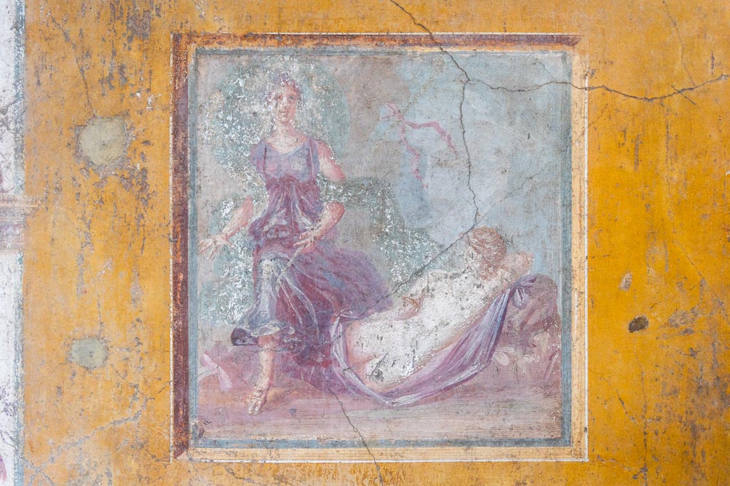VI.16.15 Pompeii. January 2024. Room F, central painting of The Sleeping Ariadne, from east wall. Photo courtesy of Johannes Eber.
Kuivalainen describes –
“A composition of two figures. In the foreground a sleeping almost naked female figure, with her back to the viewer; she is reclining on a stone, with her right arm supporting her head; she lies on a purple cloak which covers her legs; she has gold arm rings, and her hair is fair. On the left, another figure steps energetically over the legs of the sleeping figure. He wears sandals and a purple robe with wide drapery, and a flaring blue cloak; he carries a thyrsus with a red ribbon and possibly a bunch of leaves on top under his left arm; his head is slightly turned to the left, and his long curly hair is darkish.”
Kuivalainen comments –
“Sleeping Ariadne callipyge discovered by an effeminate Bacchus. The shadowing on his skin is broader and darker than the female’s. The flaring cloak resembles that of Bacchus, e.g. in the Casa del Citarista (E7), referring to velificatio and to the epiphany of the divinity.”
See Kuivalainen, I., 2021. The Portrayal of Pompeian Bacchus. Commentationes Humanarum Litterarum 140. Helsinki: Finnish Society of Sciences and Letters, (p.143, E3).