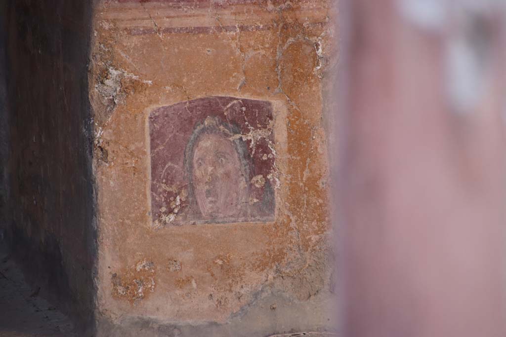VI.16.15 Pompeii. September 2021.
Atrium B, wall painting of face or mask between doorway to room E and room D at base of pilaster. Photo courtesy of Klaus Heese.