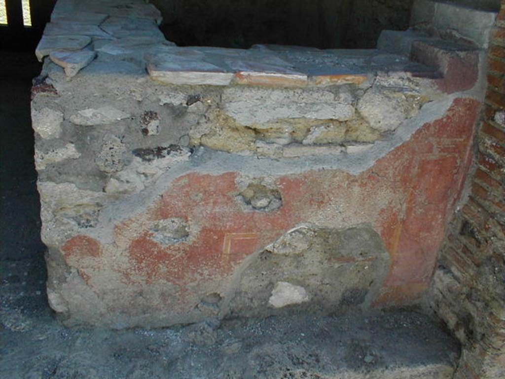 VI.16.33 Pompeii. May 2005. Remaining painted plaster on west-facing exterior side of counter. According to NdS, the outer surface of this counter had a red background. On the surface facing the road, according to Sogliano, obscene paintings were discovered. In the centre, in a yellow frame, was a large erect phallus. On each side, a male figure could be seen facing towards the centre panel and each other. The figure on the right was better preserved, and bald. There were also other painted panels and arabesques.See Notizie degli Scavi di Antichit�, 1908, (p.289).
