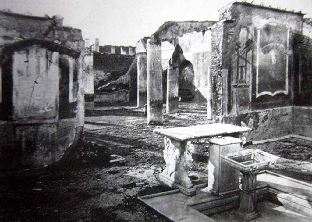 VII.1.25 Pompeii. Old undated 19th century photo. Looking north-west across atrium 24.
According to Breton, via a prothyrum paved in opus signinum patterned symmetrically with small white stones, we enter the Tuscan atrium; at the centre is a very pretty impluvium of marble at the top of which is a covered square cippus of marble with a lead pipe who poured water into a basin on a small base of marble adorned with large acanthus leaves. The fountain is accompanied by a white marble table with two feet of very fine workmanship, each composed of the anterior part of a chimera and a griffon. On the side top of the table is engraved the number LXXIX and we found a small bronze group representing Hercules armed with his club and a young Phrygian kneeling in front of him.
See Breton, Ernest. 1855. Pompeia, décrite et dessine: Seconde édition . Paris, Baudry, p. 316.