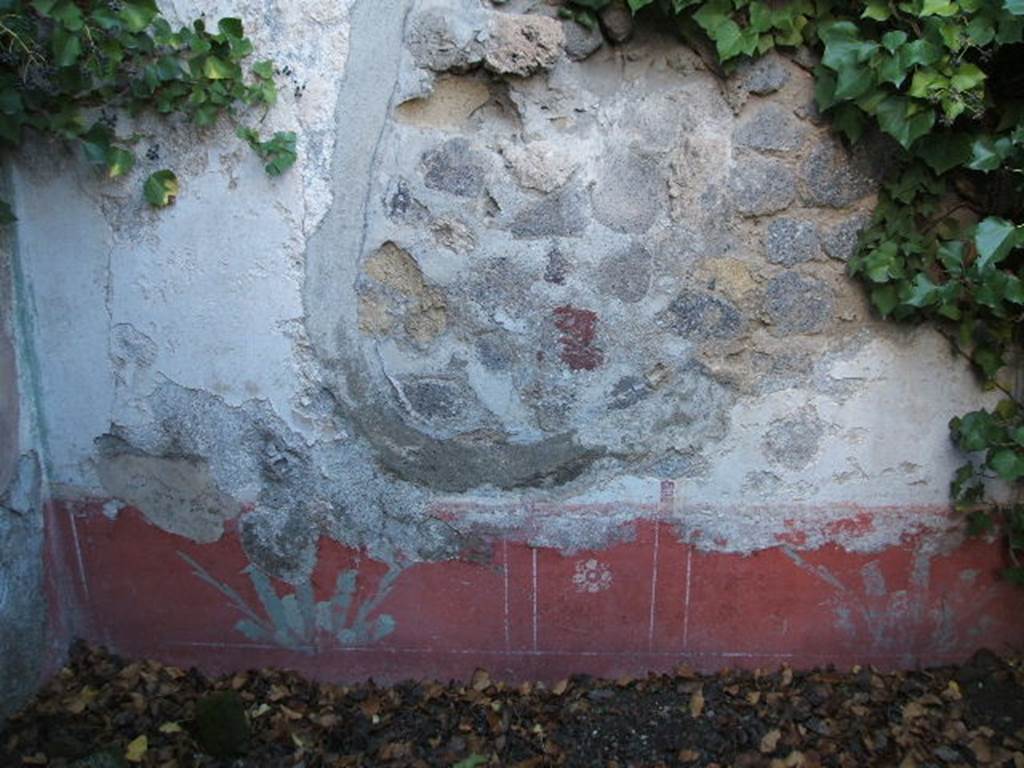 VII.2.6 Pompeii. December 2004. Painted wall decoration on north wall of cubiculum in north-west corner of atrium. The north wall had a red zoccolo, with a central compartment containing a painted rosette with four petals, in the two side panels were painted plants. The middle zone was painted white. All the walls of this room seemed to have a similar scheme but were faded and most of the plaster was missing. Found here were, among others, a panel of a “Cupid with a bunch of grapes held high in the right hand” (Sogl. 285), and a “female crowned figure, naked except for a veil that fell from her arms behind her shoulders, carrying a face in the right hand and a basket of flowers in the left hand” (Sogl. 795).
See Sogliano, A., 1879. Le pitture murali campane scoverte negli anni 1867-79. Napoli: Giannini. (Sog. p.56, no. 285, and p. 155, no.795).