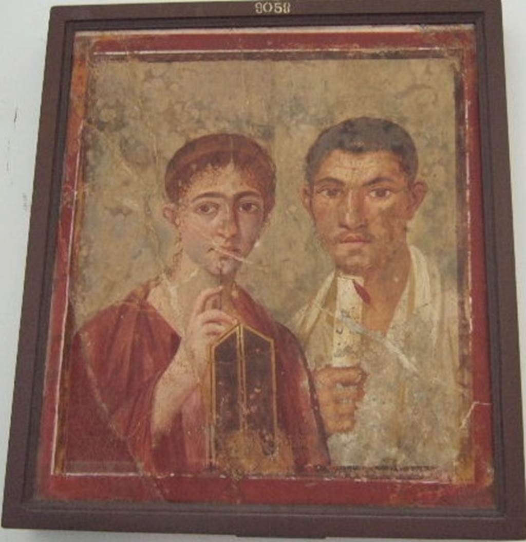 VII.2.6 Pompeii. Portrait of Terentius Neo and his wife. Found on north wall of exedra/tablinum in centre of north side of atrium. Now in Naples Archaeological Museum. Inventory number: 9058.
In the upper zone of the painted architecture was a fresco of Cupid and Psyche. The red zoccolo showed a painted plant in the centre panel, and painted garlands with peacocks on them in the side panels. In the middle zone of the wall, the central panel was painted white, which separated the two yellow side panels.
In one of these side panels, “but already very faded and nearly vanished” was the painting of “Nike standing on a shelf, and carrying a trophy on his left shoulder”.