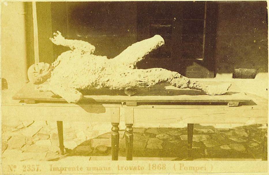 VII.2.16 Pompeii. One of the seven skeletons found in the house on 12th March 1868. Photo courtesy of Rick Bauer. Seven skeletons were found, but six of them had not left enough imprint in the cinders to make a good plaster cast. The above was the only successful one, although his left leg was not cast, on his face was a look of horror.
See Garcia y Garcia, L., 2006. Danni di guerra a Pompei. Rome: L’Erma di Bretschneider. (p.190)
According to Dwyer, the cast was only partially successful as the cavity had been infiltrated by lapilli and this left the skull and left leg exposed.
This cast, known as the Fifth Victim, was placed in the Archaeological School, and it was here that Ernest Breton saw it, and described
“This unfortunate was discovered lying on his stomach in a room to the left of the atrium of the House of Gavius Rufus. Six other skeletons were near him” from Breton, 1869.
See Dwyer, E., 2010. Pompeii’s Living Statues. Ann Arbor: Univ of Michigan Press. (p. 80)