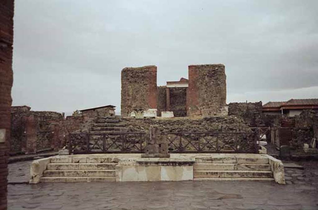 VII.4.1 Pompeii. May 2010. Looking east from Via del Foro. Photo courtesy of Rick Bauer.
Two small staircases of four steps led up from the via on each end. These led to a platform and were on either side of a rectangular altar.
After this platform, another nine steps led up to the pronaos or entrance hall to the temple. 
These steps were all found in a ruined state, but the ones on the left had been restored by the time Breton wrote in 1870.
Originally this podium would have had four white marble Corinthian columns across its façade, together with another column and pillar behind on either side.
Three capitals from these columns have been found, together with other architectural elements all in white marble.
See Breton, Ernest. 1870. Pompeia, Guide de visite a Pompei, 3rd ed. Paris, Guerin. 
