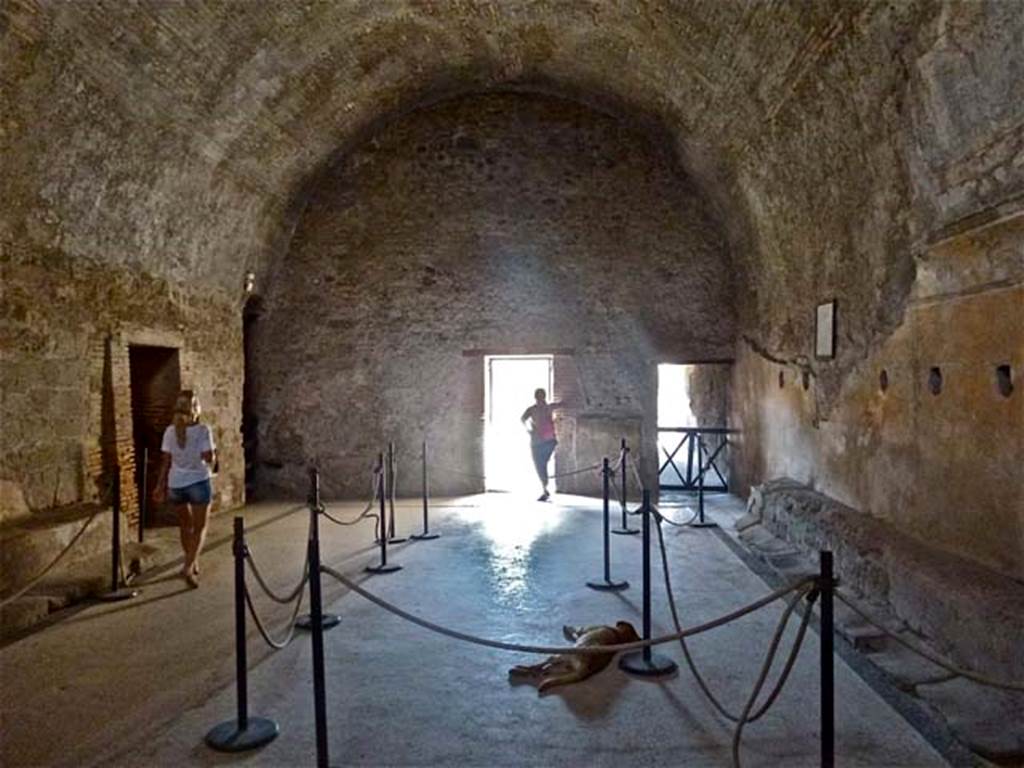 VII.5.24 Pompeii. June 2012. Men’s baths apodyterium or changing room (14), looking north.
Photo courtesy of Michael Binns.
According to Fiorelli –
The changing room (14), other than the doorway from the fauces (corridor 16, on right above), had another five doorways around it.
On the right of the corridor 16, (centre, above) was a small room where the oils and ointments were stored.
On the left of the photo above (west) was the doorway to the long corridor leading to the boiler area.
On the left (behind the figure) was also the third doorway which led into the tepidarium (37).
The fourth doorway (in the south-west corner) led into the frigidarium (19)
The fifth doorway (in the south-east corner) led into corridor 13, leading towards the garden/courtyard area, which had two secondary entrances or exits towards the east and west sides of the Insula.
See Pappalardo, U., 2001. La Descrizione di Pompei per Giuseppe Fiorelli (1875). Napoli: Massa Editore. (p.94-95).