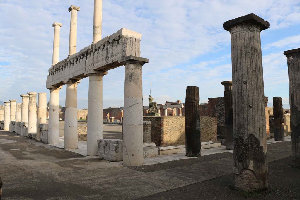 VII.8 Pompeii Forum. December 2018. Looking north-east from south-west corner. Photo courtesy of Aude Durand.
On the west side, centre left, the columns of the Forum were replaced. On the south side, on the right, the original columns of the portico still remains.
“The ancient portico of the Forum of Pompeii, of tufa covered with stucco, of Greek (Doric) style, in later times was largely replaced, or it probably all had to be, by a portico in that limestone, called travertine in Naples, of heavier and less beautiful form, but of more solid and perfect construction.
On the entire west side, the ancient portico was demolished – still recognizable by the bases remaining in place – and they built or began to build the new one. On the south side, and on that part of the east side that is south of the road called Via dell'Abbondanza, the ancient portico remained.”
(L’antico portico del Foro di Pompei, di tufo rivestito di stucco, di stile greco (dorico), in epoca posteriore fu in gran parte rimpiazzato, o doveva esserlo probabilmente tutto, da un portico in quella pietra calcare che a Napoli si chiama travertino di forme più pesanti e poco belle, ma di costruzione più solida e perfetta. Sul intera lato ovest fu demolito l’antico portico – riconoscibile ancora dalle basi rimaste al posto – e costruito, o cominciato a costruire quello nuovo. Sul lato sud, e su quello parte del lato est che sta a sud della strada detta – dell’Abbondanza, rimase il portico antico.)
See Mau, in Bullettino dell’Instituto di Corrispondenza Archeologica (DAIR), 06, 1891, (p.168).