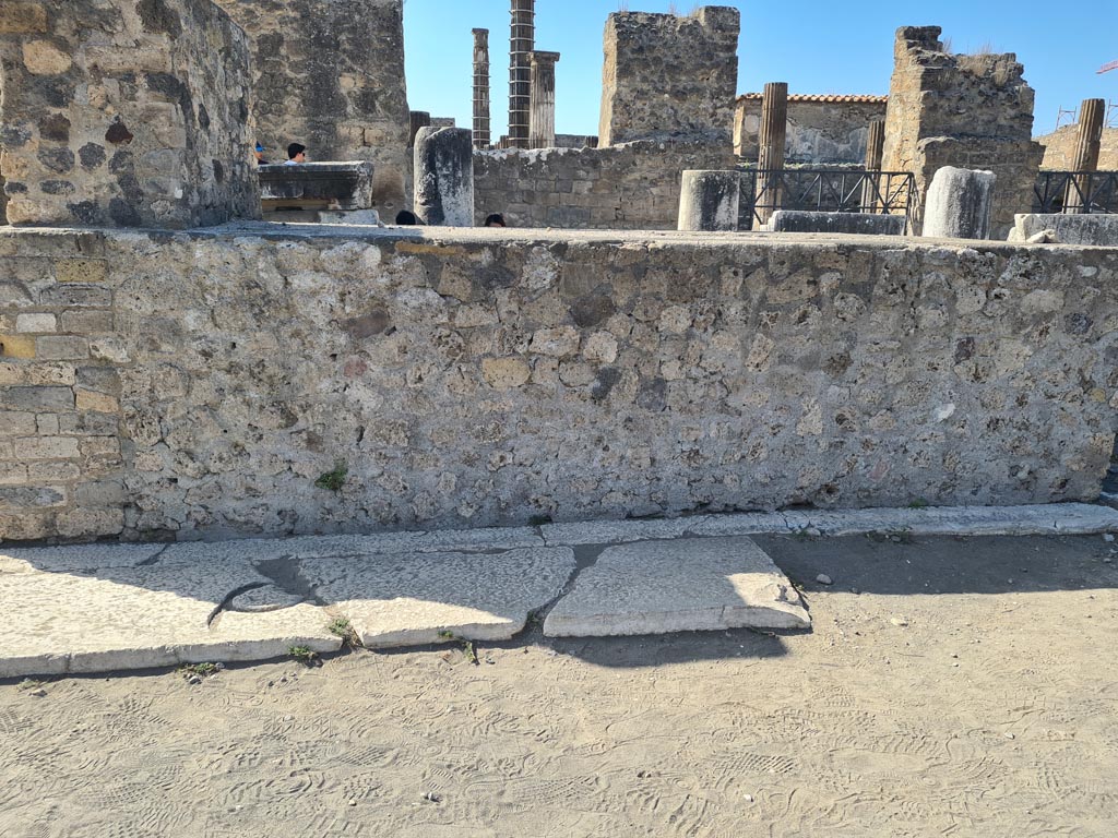 VII.8 Pompeii Forum. October 2023.
Looking towards east side of base with remaining letter Q, still visible. Photo courtesy of Klaus Heese.
According to Van Buren – The Great Inscription of the Pavement of the Forum.
“It is well known that the pavement of the Forum was paved, about the beginning of the first century AD, with large blocks of limestone, well laid, and that at present, while considerable portions of this pavement are preserved at the north and south ends, the open space in the centre has been denuded except for a few isolated blocks. This pavement antedates the original construction of the limestone portico, which was in process of construction in 63AD and had been begun or at least was contemplated under Tiberius; it is earlier than the bases of equestrian statues along the west side of the Forum, since these were constructed upon it; and it is earlier than some, but later than others, of the bases of equestrian statues along the north and south ends of the Forum.
The reason for the disappearance of most of the central portion of this fine pavement is to be sought in the activities of the survivors after the eruption of 79: the Forum, like the Amphitheatre and the great theatre, could easily be found, and it furnished too valuable a quarry of building materials to be left unworked.
It has not been recognised however that this pavement contained a great inscription, in letters of bronze set into the limestone blocks, and running from the west to the east side of the Forum.
Of this monumental inscription there survives in position only the cutting for the first letter, a Q, in a block of the pavement immediately to the east of the very large oblong statue base which is situated at about the middle of the west side of the Forum (see Plan fig 1, Note 3 below).
This one letter, given its character and position, is ample evidence of the former existence of the whole inscription: similar pavements containing similar inscriptions have been preserved in at least three instances.”
See Van Buren, A. W., 1918. The Forum at Pompeii in MAAR Vol II, p. 71 (and note 3, below).
