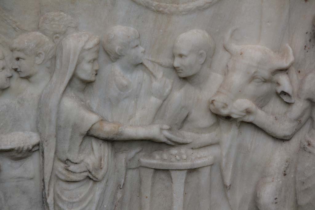 VII.9.2 Pompeii. April 2014. Detail from west side of Altar. Photo courtesy of Klaus Heese.
According to Mau, a priest with a toga drawn over his head pours a libation from a shallow bowl or patera onto an altar which is in the form of a tripod.
On the right the victimarius or slayer and an assistant are bringing a bull to the altar for sacrifice.
See Mau, A., 1907, translated by Kelsey F. W. Pompeii: Its Life and Art. New York: Macmillan. (Pages 106-7).