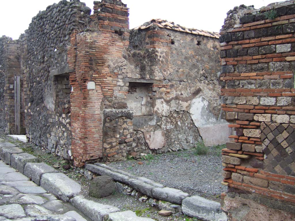 VII.10.2 Pompeii. December 2005. Entrance doorway on Vicolo d’Eumachia, looking north.
According to Eschebach on the left of the entrance would have been the shop podium or counter, with shelves or steps above it.
See Eschebach, L., 1993. Gebäudeverzeichnis und Stadtplan der antiken Stadt Pompeji. Köln: Böhlau. (p.319)
According to Boyce, in the north wall was a large rectangular niche with a narrow shelf-like projection beside it on the left.
Fiorelli called it “un larario”.
Fiorelli, Descrizione, 273.
See Boyce G. K., 1937. Corpus of the Lararia of Pompeii. Rome: MAAR 14. (p.69, no.306).