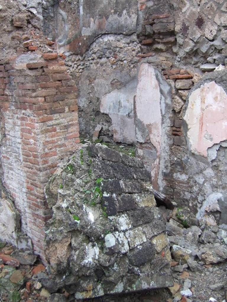 VII.10.3 Pompeii. December 2005. Doorway to room 4, in north-west corner of atrium.
The doorway would have led into a room, described as a triclinium, originally with flooring of a reddish cocciopesto. The door threshold was formed by two square slabs of travertine and inserted in its south end was a small slab of grey marble. Seen on each of the smooth surface of the slabs, was a circular recess for the fixing of the double-door hinges. (p.54)
The floor was upgraded to a black and white mosaic. The walls were redecorated in the IVth style. The black zoccolo (dado/plinth) showed alternative narrow panels with rosettes, in the centre were plants motifs. The middle zone on each wall showed an edicula panel, painted white which contained a pinax, no longer visible. The side panels were painted red, edged by a simple bordered band.
Studi della Soprintendenza archeologica di Pompei, 22: l”Insula VII, 10 di Pompei, by Angelo Amoroso, (p.54 and p.74)
According to Bragantini, on the north-east side the mosaic was visible, whilst on the south-east side the cocciopesto was visible.
See Bragantini, de Vos, Badoni, 1986. Pitture e Pavimenti di Pompei, Parte 3. Rome: ICCD. (p.179)