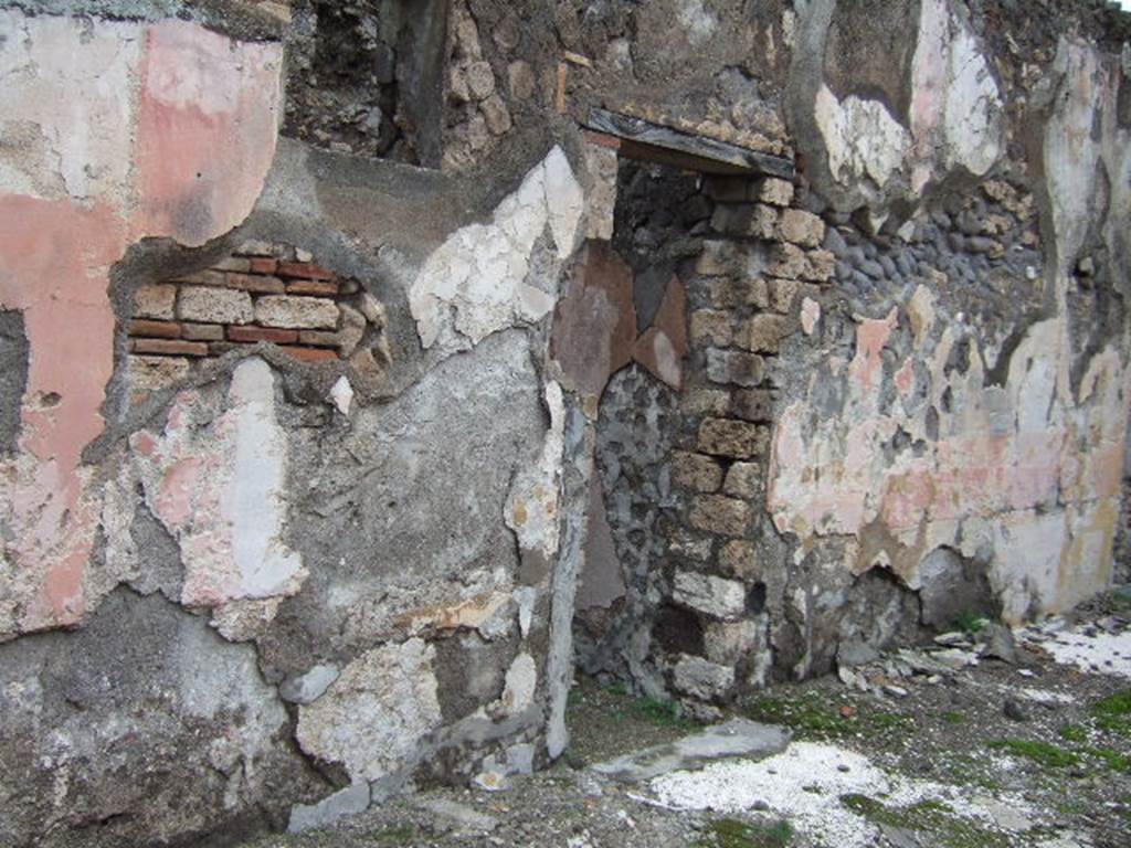 VII.10.3 Pompeii. December 2005. Doorway to room 6, a cubiculum on north side of atrium.
This room also had a floor of cocciopesto, joined in the doorway to the threshold which was formed by two rectangular travertine slabs, marked in the centre with a circular recess for the fixing of the double-door hinges. When redecorated the walls were repainted with plaster panels edged with a red line, of which some traces remain. The middle of the walls had vertical panels separated by architectural paintings, the central panels were yellow, the sides being red. The zoccolo was painted with plant motifs on a red background. The upper part of the walls was painted white. Its original flooring was kept.
Studi della Soprintendenza archeologica di Pompei, 22: l”Insula VII, 10 di Pompei, by Angelo Amoroso, (p.54 and p.74)