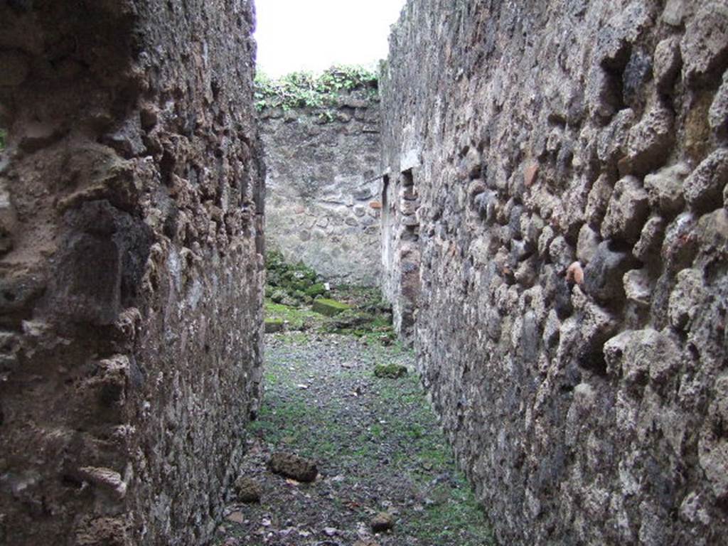 VII.10.3 Pompeii. December 2005. Corridor 18, looking south into room 19, the kitchen.
Directly ahead, in the south-west corner of the kitchen, was a small separate latrine. According to Boyce, in the kitchen was a lararium painting upon a white background, depicting Fortuna. In her left hand she held a rudder, her right hand extended above a globe which lay at her feet. The painting was incomplete, for on the right side the stucco showed that at least one more figure was to have been added.
Helbig 74.
See Boyce G. K., 1937. Corpus of the Lararia of Pompeii. Rome: MAAR 14. (p.69, no.308)
According to Amoroso, from these service rooms, it was possible to exit the house in the direction of the Vicolo degli Scheletri, without entering the main house. The east wall of the kitchen was enriched with the remains of the lararium, the figure of a divinity could be seen, but today is not visible.
Studi della Soprintendenza archeologica di Pompei, 22: l”Insula VII, 10 di Pompei, by Angelo Amoroso, (p.77)