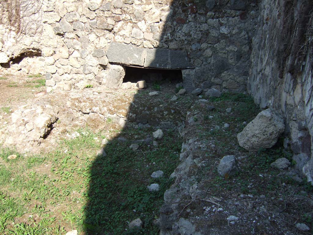 VII.12.7 Pompeii. September 2005. Looking east to remains of oven and workbench near south wall.
According to Boyce, on the south wall of the room with the oven was a large lararium painting.
In the centre was a blazing tripod, with the Genius to the right of it.
On each side was a wreathed Lar.
To the left of this group stood Vesta, at her side was an ass with a bell around its neck.
On the right of the group stood Mercury.
In the lower zone, marked off from the upper by a brownish stripe, were the two serpents.
They were approaching a gold-coloured altar, on top of which was a white shallow dish containing a blazing fire.
In the fire was an egg and several fruits – a date, a pomegranate and a medlar.
See Boyce G. K., 1937. Corpus of the Lararia of Pompeii. Rome: MAAR 14. (p.70, no.313)
See Helbig, W., 1868. Wandgemälde der vom Vesuv verschütteten Städte Campaniens. Leipzig: Breitkopf und Härtel. (68)
According to BdI, this was the first time that Mercury appeared associated with the Lares, in Pompeii.
See Bullettino dell’Instituto di Corrispondenza Archeologica (DAIR), 1864, p.114-115 (described as Casa II.)