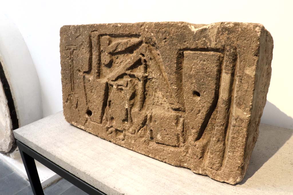 VII.15.1/2 Pompeii. February 2021.
Limestone relief signed by the master builder (structor) Diogenes depicting –
a trowel, an apotropaic phallus, a plumbline, a cudgel or an axe/a hammer that cuts orthogonally, a scalpel and two unidentifiable objects.
On display in Antiquarium at VIII.1.4 but found on the west perimeter wall of the house at VII.1.52, on Via dei Soprastanti.
Photo courtesy of Fabien Bièvre-Perrin (CC BY-NC-SA).